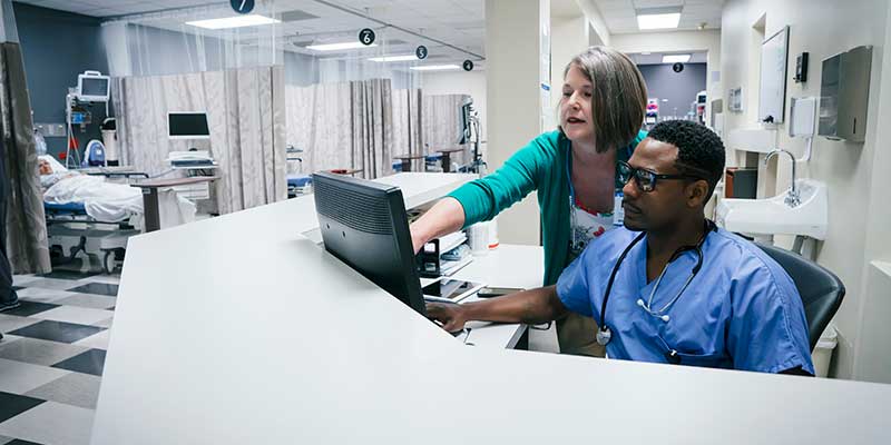 Doctor and nurse reviewing digital patient records, in a hospital wing