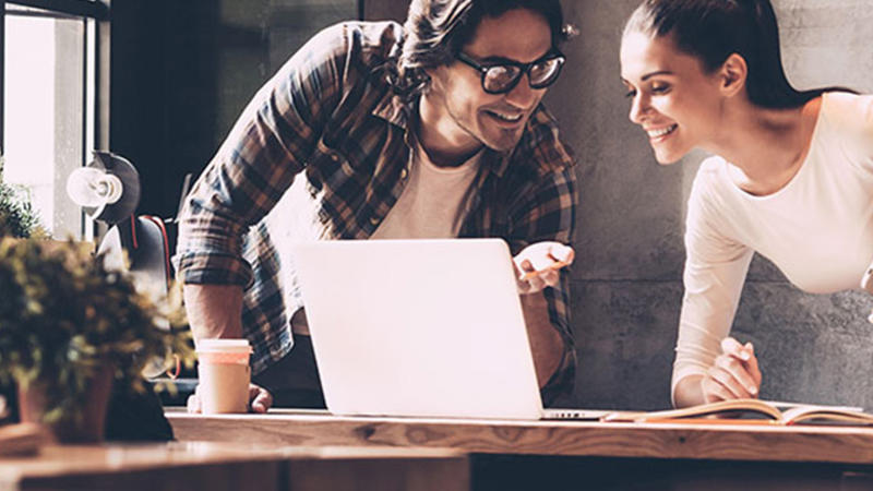A man and a woman leaning on a table, looking at a laptop