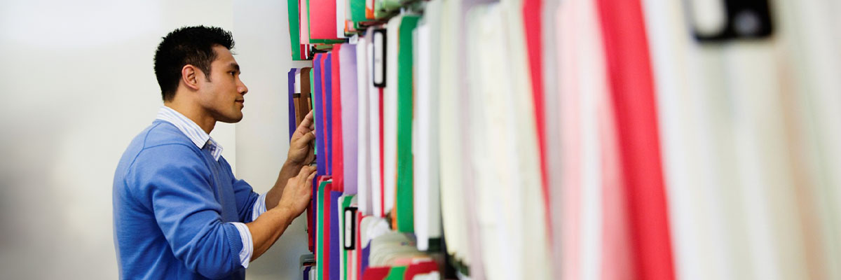 Man standing at filing cabinet looking at folders.