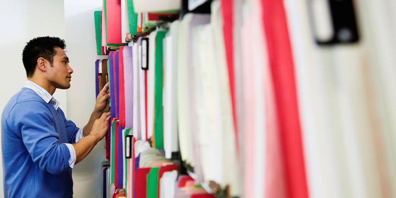 Man standing at filing cabinet looking at folders.