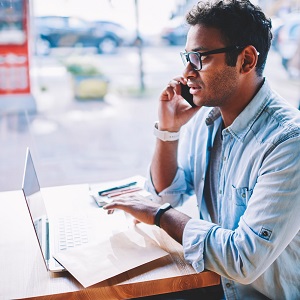 Man talking on phone at a car dealership while typing on a laptop