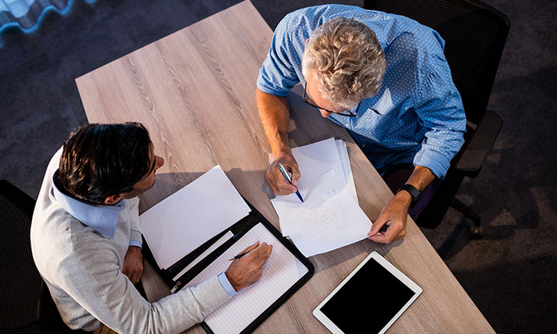 Birds eye view of two men meeting taking notes on paper.