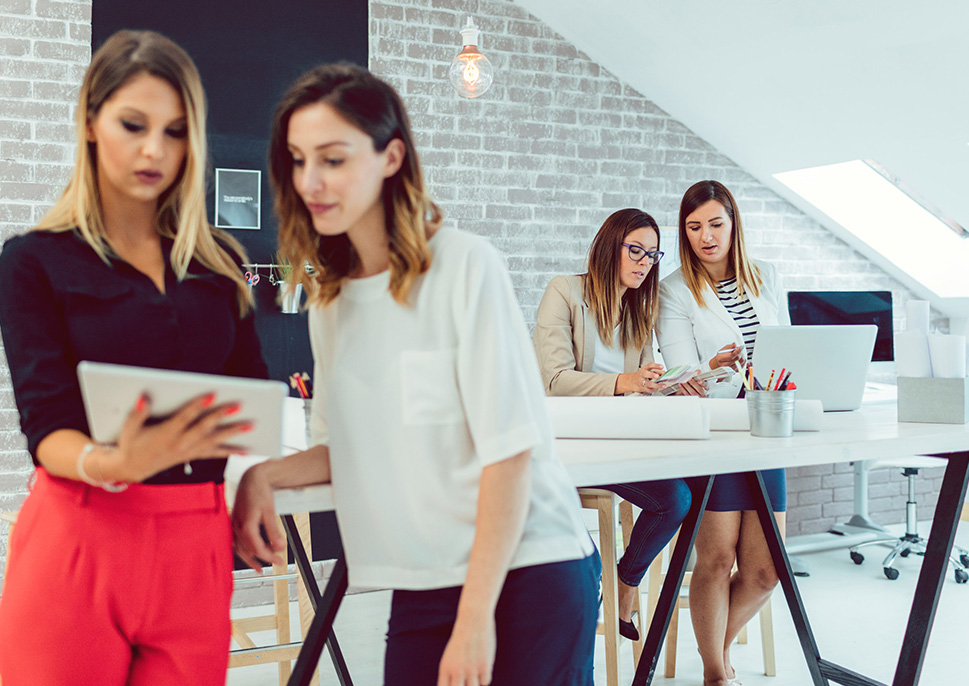 Two women in an open office looking at a tablet